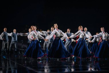 Valmiera, Letonya - 7 Haziran 2025 - GAUJA 80 'deki geleneksel Letonya halk dansları kolajı, renkli kostümlü dansçıları gece aydınlatmalı bir sahnede sergiliyorlar..