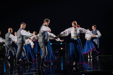 Valmiera, Letonya - 7 Haziran 2025 - GAUJA 80 'deki geleneksel Letonya halk dansları kolajı, renkli kostümlü dansçıları gece aydınlatmalı bir sahnede sergiliyorlar..