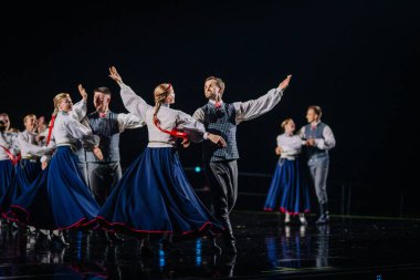 Valmiera, Letonya - 7 Haziran 2025 - GAUJA 80 'deki geleneksel Letonya halk dansları kolajı, renkli kostümlü dansçıları gece aydınlatmalı bir sahnede sergiliyorlar..