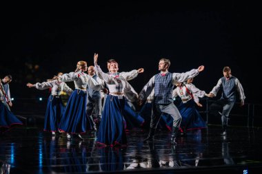 Valmiera, Letonya - 7 Haziran 2025 - GAUJA 80 'deki geleneksel Letonya halk dansları kolajı, renkli kostümlü dansçıları gece aydınlatmalı bir sahnede sergiliyorlar..