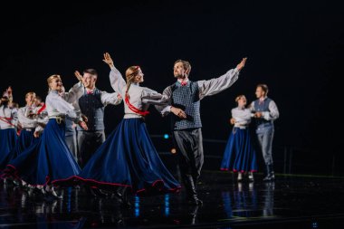 Valmiera, Letonya - 7 Haziran 2025 - GAUJA 80 'deki geleneksel Letonya halk dansları kolajı, renkli kostümlü dansçıları gece aydınlatmalı bir sahnede sergiliyorlar..