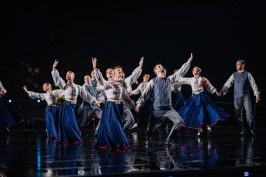 Valmiera, Letonya - 7 Haziran 2025 - GAUJA 80 'deki geleneksel Letonya halk dansları kolajı, renkli kostümlü dansçıları gece aydınlatmalı bir sahnede sergiliyorlar..