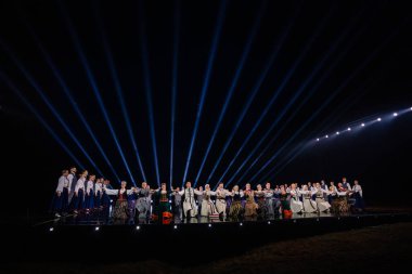 Valmiera, Letonya - 7 Haziran 2025 - GAUJA 80 'deki geleneksel Letonya halk dansları kolajı, renkli kostümlü dansçıları gece aydınlatmalı bir sahnede sergiliyorlar..