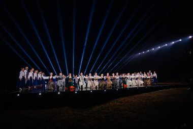 Valmiera, Letonya - 7 Haziran 2025 - GAUJA 80 'deki geleneksel Letonya halk dansları kolajı, renkli kostümlü dansçıları gece aydınlatmalı bir sahnede sergiliyorlar..
