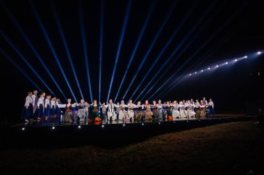 Valmiera, Letonya - 7 Haziran 2025 - GAUJA 80 'deki geleneksel Letonya halk dansları kolajı, renkli kostümlü dansçıları gece aydınlatmalı bir sahnede sergiliyorlar..