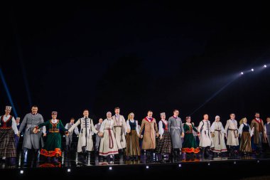Valmiera, Letonya - 7 Haziran 2025 - GAUJA 80 'deki geleneksel Letonya halk dansları kolajı, renkli kostümlü dansçıları gece aydınlatmalı bir sahnede sergiliyorlar..