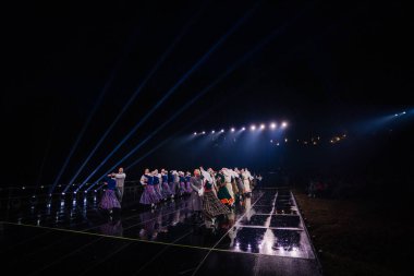 Valmiera, Letonya - 7 Haziran 2025 - GAUJA 80 'deki geleneksel Letonya halk dansları kolajı, renkli kostümlü dansçıları gece aydınlatmalı bir sahnede sergiliyorlar..