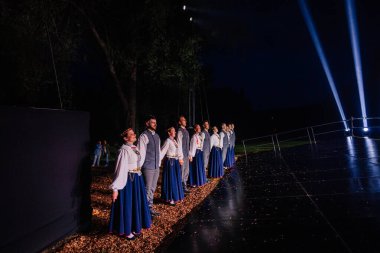 Valmiera, Letonya - 7 Haziran 2025 - GAUJA 80 'deki geleneksel Letonya halk dansları kolajı, renkli kostümlü dansçıları gece aydınlatmalı bir sahnede sergiliyorlar..