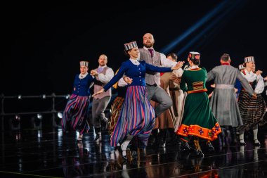 Valmiera, Letonya - 7 Haziran 2025 - GAUJA 80 'deki geleneksel Letonya halk dansları kolajı, renkli kostümlü dansçıları gece aydınlatmalı bir sahnede sergiliyorlar..