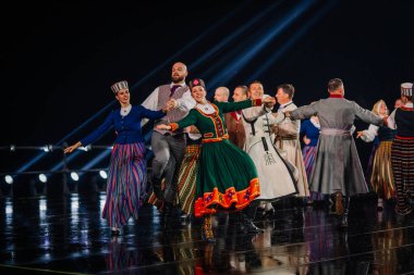Valmiera, Letonya - 7 Haziran 2025 - GAUJA 80 'deki geleneksel Letonya halk dansları kolajı, renkli kostümlü dansçıları gece aydınlatmalı bir sahnede sergiliyorlar..