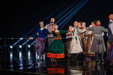 Valmiera, Letonya - 7 Haziran 2025 - GAUJA 80 'deki geleneksel Letonya halk dansları kolajı, renkli kostümlü dansçıları gece aydınlatmalı bir sahnede sergiliyorlar..
