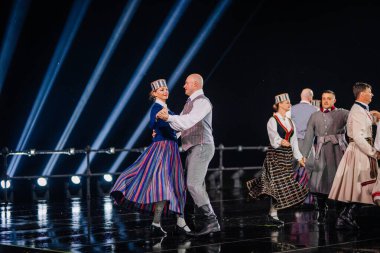 Valmiera, Letonya - 7 Haziran 2025 - GAUJA 80 'deki geleneksel Letonya halk dansları kolajı, renkli kostümlü dansçıları gece aydınlatmalı bir sahnede sergiliyorlar..