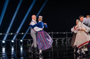 Valmiera, Letonya - 7 Haziran 2025 - GAUJA 80 'deki geleneksel Letonya halk dansları kolajı, renkli kostümlü dansçıları gece aydınlatmalı bir sahnede sergiliyorlar..