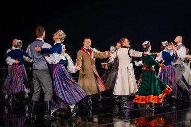 Valmiera, Letonya - 7 Haziran 2025 - GAUJA 80 'deki geleneksel Letonya halk dansları kolajı, renkli kostümlü dansçıları gece aydınlatmalı bir sahnede sergiliyorlar..