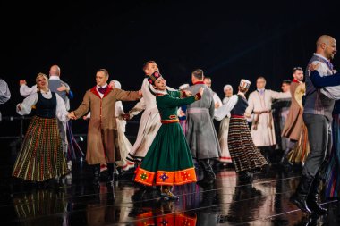 Valmiera, Letonya - 7 Haziran 2025 - GAUJA 80 'deki geleneksel Letonya halk dansları kolajı, renkli kostümlü dansçıları gece aydınlatmalı bir sahnede sergiliyorlar..