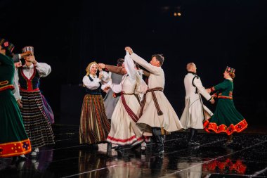 Valmiera, Letonya - 7 Haziran 2025 - GAUJA 80 'deki geleneksel Letonya halk dansları kolajı, renkli kostümlü dansçıları gece aydınlatmalı bir sahnede sergiliyorlar..