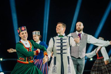 Valmiera, Letonya - 7 Haziran 2025 - GAUJA 80 'deki geleneksel Letonya halk dansları kolajı, renkli kostümlü dansçıları gece aydınlatmalı bir sahnede sergiliyorlar..