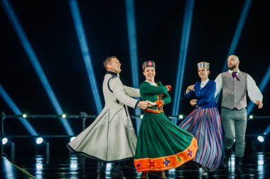 Valmiera, Letonya - 7 Haziran 2025 - GAUJA 80 'deki geleneksel Letonya halk dansları kolajı, renkli kostümlü dansçıları gece aydınlatmalı bir sahnede sergiliyorlar..