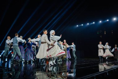 Valmiera, Letonya - 7 Haziran 2025 - GAUJA 80 'deki geleneksel Letonya halk dansları kolajı, renkli kostümlü dansçıları gece aydınlatmalı bir sahnede sergiliyorlar..