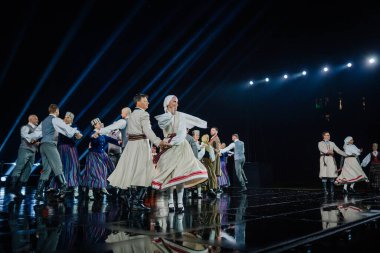 Valmiera, Letonya - 7 Haziran 2025 - GAUJA 80 'deki geleneksel Letonya halk dansları kolajı, renkli kostümlü dansçıları gece aydınlatmalı bir sahnede sergiliyorlar..
