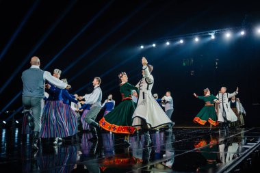 Valmiera, Letonya - 7 Haziran 2025 - GAUJA 80 'deki geleneksel Letonya halk dansları kolajı, renkli kostümlü dansçıları gece aydınlatmalı bir sahnede sergiliyorlar..