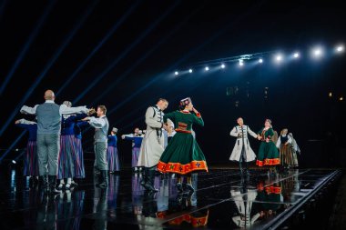 Valmiera, Letonya - 7 Haziran 2025 - GAUJA 80 'deki geleneksel Letonya halk dansları kolajı, renkli kostümlü dansçıları gece aydınlatmalı bir sahnede sergiliyorlar..