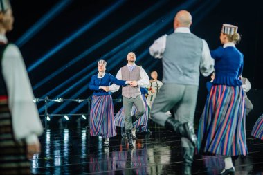 Valmiera, Letonya - 7 Haziran 2025 - GAUJA 80 'deki geleneksel Letonya halk dansları kolajı, renkli kostümlü dansçıları gece aydınlatmalı bir sahnede sergiliyorlar..