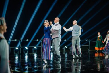 Valmiera, Letonya - 7 Haziran 2025 - GAUJA 80 'deki geleneksel Letonya halk dansları kolajı, renkli kostümlü dansçıları gece aydınlatmalı bir sahnede sergiliyorlar..