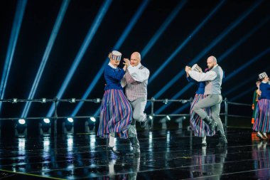 Valmiera, Letonya - 7 Haziran 2025 - GAUJA 80 'deki geleneksel Letonya halk dansları kolajı, renkli kostümlü dansçıları gece aydınlatmalı bir sahnede sergiliyorlar..