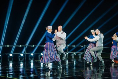 Valmiera, Letonya - 7 Haziran 2025 - GAUJA 80 'deki geleneksel Letonya halk dansları kolajı, renkli kostümlü dansçıları gece aydınlatmalı bir sahnede sergiliyorlar..