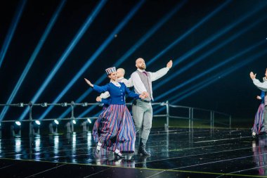 Valmiera, Letonya - 7 Haziran 2025 - GAUJA 80 'deki geleneksel Letonya halk dansları kolajı, renkli kostümlü dansçıları gece aydınlatmalı bir sahnede sergiliyorlar..