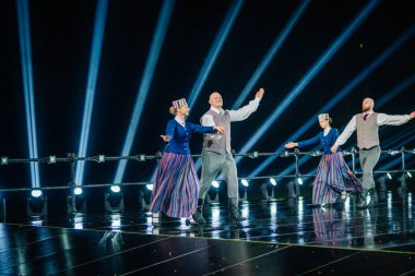 Valmiera, Letonya - 7 Haziran 2025 - GAUJA 80 'deki geleneksel Letonya halk dansları kolajı, renkli kostümlü dansçıları gece aydınlatmalı bir sahnede sergiliyorlar..