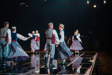 Valmiera, Letonya - 7 Haziran 2025 - GAUJA 80 'deki geleneksel Letonya halk dansları kolajı, renkli kostümlü dansçıları gece aydınlatmalı bir sahnede sergiliyorlar..