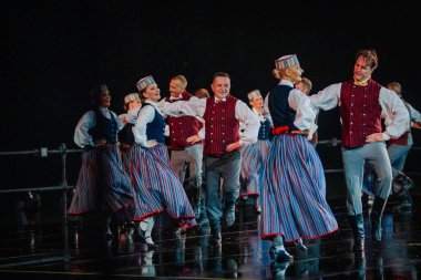 Valmiera, Letonya - 7 Haziran 2025 - GAUJA 80 'deki geleneksel Letonya halk dansları kolajı, renkli kostümlü dansçıları gece aydınlatmalı bir sahnede sergiliyorlar..