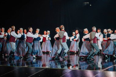 Valmiera, Letonya - 7 Haziran 2025 - GAUJA 80 'deki geleneksel Letonya halk dansları kolajı, renkli kostümlü dansçıları gece aydınlatmalı bir sahnede sergiliyorlar..