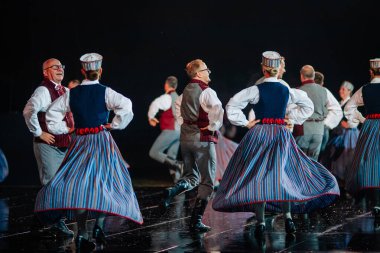 Valmiera, Letonya - 7 Haziran 2025 - GAUJA 80 'deki geleneksel Letonya halk dansları kolajı, renkli kostümlü dansçıları gece aydınlatmalı bir sahnede sergiliyorlar..