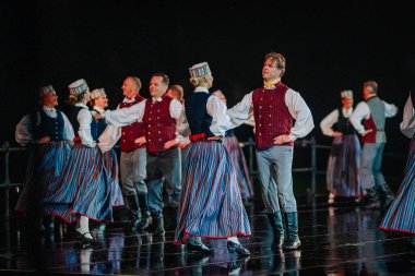 Valmiera, Letonya - 7 Haziran 2025 - GAUJA 80 'deki geleneksel Letonya halk dansları kolajı, renkli kostümlü dansçıları gece aydınlatmalı bir sahnede sergiliyorlar..