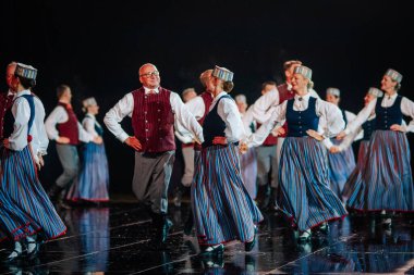 Valmiera, Letonya - 7 Haziran 2025 - GAUJA 80 'deki geleneksel Letonya halk dansları kolajı, renkli kostümlü dansçıları gece aydınlatmalı bir sahnede sergiliyorlar..
