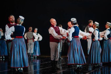 Valmiera, Letonya - 7 Haziran 2025 - GAUJA 80 'deki geleneksel Letonya halk dansları kolajı, renkli kostümlü dansçıları gece aydınlatmalı bir sahnede sergiliyorlar..