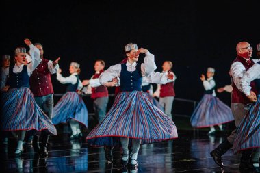Valmiera, Letonya - 7 Haziran 2025 - GAUJA 80 'deki geleneksel Letonya halk dansları kolajı, renkli kostümlü dansçıları gece aydınlatmalı bir sahnede sergiliyorlar..