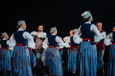 Valmiera, Letonya - 7 Haziran 2025 - GAUJA 80 'deki geleneksel Letonya halk dansları kolajı, renkli kostümlü dansçıları gece aydınlatmalı bir sahnede sergiliyorlar..