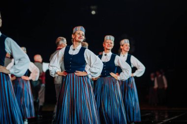 Valmiera, Letonya - 7 Haziran 2025 - GAUJA 80 'deki geleneksel Letonya halk dansları kolajı, renkli kostümlü dansçıları gece aydınlatmalı bir sahnede sergiliyorlar..