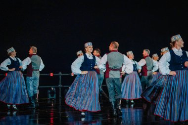 Valmiera, Letonya - 7 Haziran 2025 - GAUJA 80 'deki geleneksel Letonya halk dansları kolajı, renkli kostümlü dansçıları gece aydınlatmalı bir sahnede sergiliyorlar..