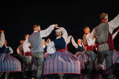 Valmiera, Letonya - 7 Haziran 2025 - GAUJA 80 'deki geleneksel Letonya halk dansları kolajı, renkli kostümlü dansçıları gece aydınlatmalı bir sahnede sergiliyorlar..