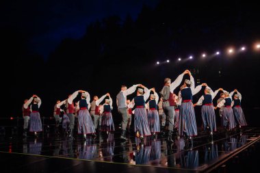 Valmiera, Letonya - 7 Haziran 2025 - GAUJA 80 'deki geleneksel Letonya halk dansları kolajı, renkli kostümlü dansçıları gece aydınlatmalı bir sahnede sergiliyorlar..
