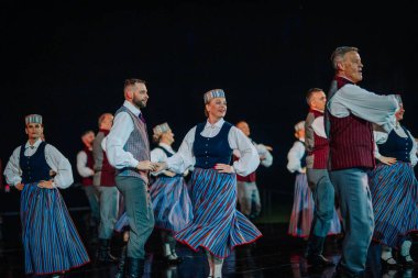 Valmiera, Letonya - 7 Haziran 2025 - GAUJA 80 'deki geleneksel Letonya halk dansları kolajı, renkli kostümlü dansçıları gece aydınlatmalı bir sahnede sergiliyorlar..