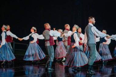 Valmiera, Letonya - 7 Haziran 2025 - GAUJA 80 'deki geleneksel Letonya halk dansları kolajı, renkli kostümlü dansçıları gece aydınlatmalı bir sahnede sergiliyorlar..