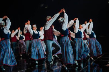 Valmiera, Letonya - 7 Haziran 2025 - GAUJA 80 'deki geleneksel Letonya halk dansları kolajı, renkli kostümlü dansçıları gece aydınlatmalı bir sahnede sergiliyorlar..
