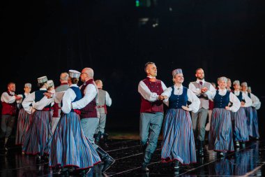 Valmiera, Letonya - 7 Haziran 2025 - GAUJA 80 'deki geleneksel Letonya halk dansları kolajı, renkli kostümlü dansçıları gece aydınlatmalı bir sahnede sergiliyorlar..