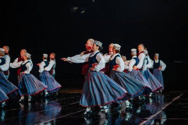 Valmiera, Letonya - 7 Haziran 2025 - GAUJA 80 'deki geleneksel Letonya halk dansları kolajı, renkli kostümlü dansçıları gece aydınlatmalı bir sahnede sergiliyorlar..